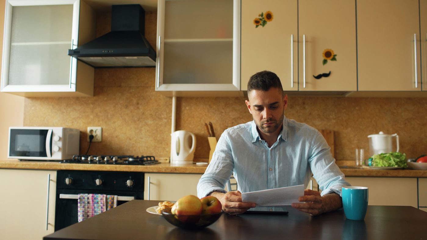Un hombre lee en la cocina la documentación de su procedimiento de deudas
